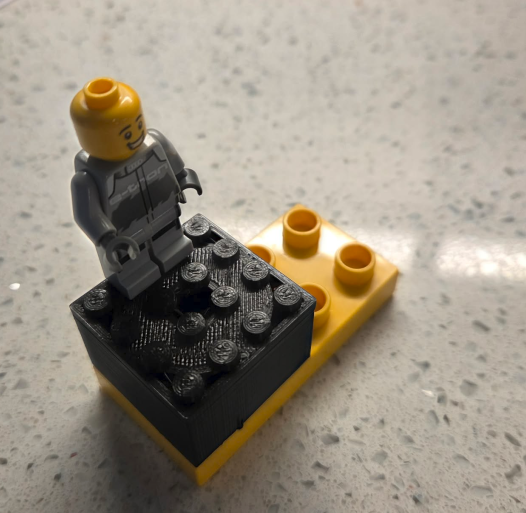 A 3D-printed Lego-compatible adapter sitting on top of a Duplo brick, with a Lego minifigure standing on it.